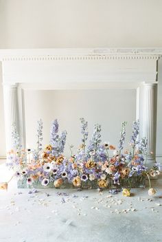 a bunch of flowers that are sitting on the ground in front of a fire place