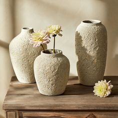 three vases sitting on top of a wooden table with flowers in them and one is empty