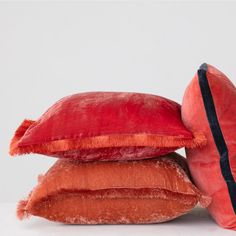 three pillows stacked on top of each other in front of a white background, one red and the other orange