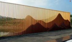 a large metal fence with mountains painted on it's side next to a body of water