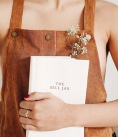 a woman in an apron holding a book with flowers on it and the words the bell jar