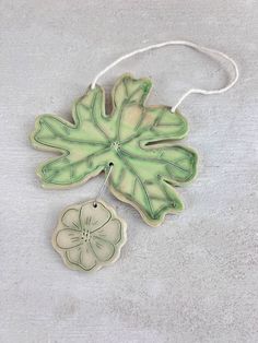 a green and white ceramic flower ornament hanging from a string on a gray surface