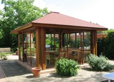 a wooden gazebo sitting in the middle of a garden next to a table and chairs