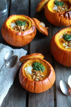 three pumpkins filled with food sitting on top of a wooden table next to spoons