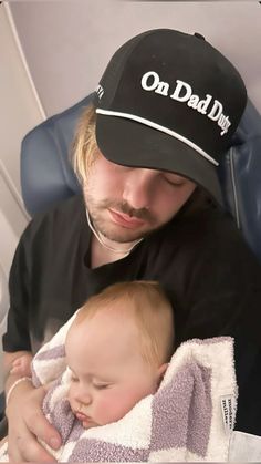 a man holding a baby wrapped in a towel and wearing a hat on his head