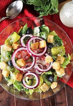 a salad with croutons, lettuce and tomatoes in a glass bowl