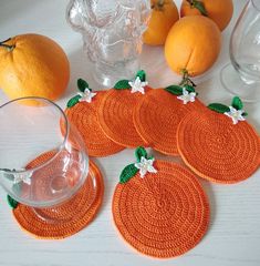 orange coasters with white flowers and green leaves are on a table next to glassware