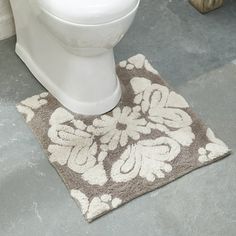 a white toilet sitting on top of a bathroom floor next to a rug with flowers