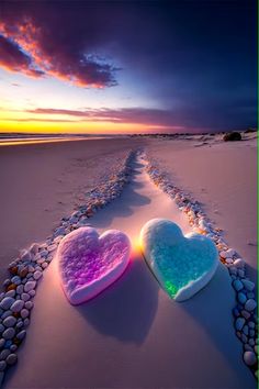 two heart shaped pillows sitting on top of a sandy beach next to the ocean at sunset