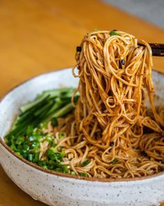 the noodles are being held by chopsticks in a white bowl on a wooden table