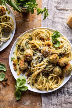 two plates of pasta with pesto and chicken meatballs on the table next to some breadcrumbs