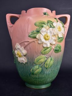 a pink vase with white flowers painted on the side and green leaves in the middle