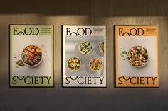 three cookbooks with food on them are shown in front of a wall that reads food society