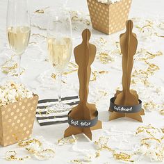 three oscar award trophies sitting on top of a table next to wine glasses and confetti