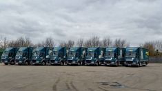 a row of semi trucks parked in a parking lot next to each other on a cloudy day