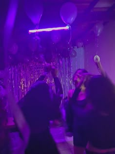 a group of people dancing in a room with balloons and streamers hanging from the ceiling