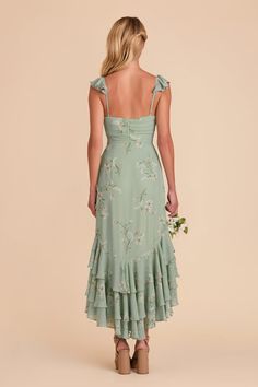 the back of a woman wearing a green dress with floral print on it and straps