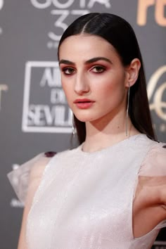 a woman with long hair wearing a white dress and large hoop earrings on her head