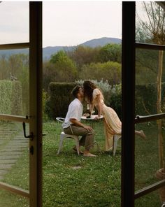 a man and woman sitting at a table in front of a window with an open door