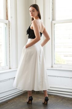 a woman standing in front of a window wearing a white and black dress with bow at the back