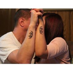 a man and woman holding hands with tattoos on their arms, looking at each other