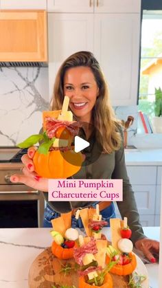 a woman holding up a pumpkin shaped cupcake on top of a wooden board in a kitchen