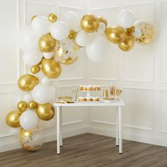 gold and white balloons are hanging from the ceiling above a table with desserts on it