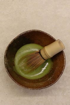 a wooden whisk in a brown bowl with green liquid