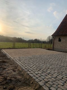 a brick driveway in front of a house with a fence and grassy field behind it