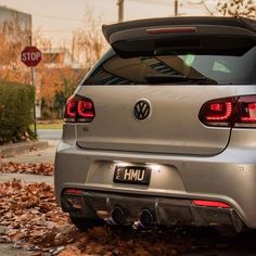 the back end of a silver car parked on leaves in front of a stop sign