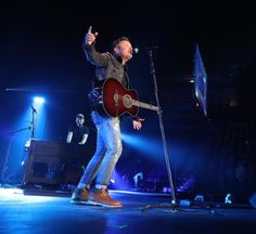 a man holding a guitar while standing on top of a stage