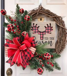 a christmas wreath is hung on the front door with red and black plaid ribbon, pineconis, and an antlers