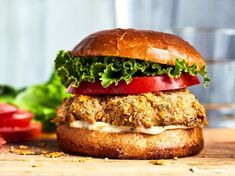 a chicken sandwich with lettuce and tomatoes on a cutting board next to tomato slices