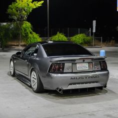 the back end of a silver sports car parked in a parking lot at night time