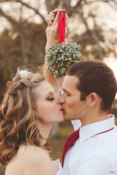 a man and woman kissing each other in front of trees with flowers on their heads