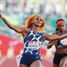 a woman with orange hair is in the middle of a race and has her arms outstretched