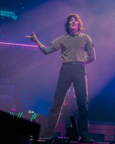 a man standing on top of a stage in front of purple and blue lights with his arms out