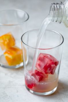 a glass filled with ice and water next to another glass full of fruit cubes