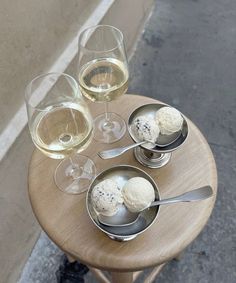 three ice creams and two wine glasses on a small table with silver spoons