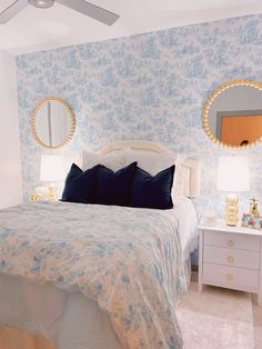 a bedroom with blue and white wallpaper, two round mirrors on each side of the bed