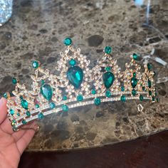 a hand holding a tiara with emeralds and diamonds on it's head