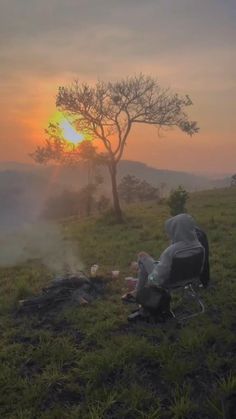 a person sitting in a chair on top of a grass covered field next to a tree