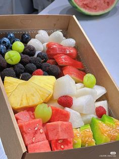 a cardboard box filled with assorted cut up fruits and watermelon wedges