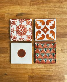 four square tiles with designs on them sitting on a wooden floor next to each other