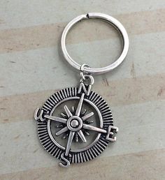 a metal keychain with a compass on the front and back ends, sitting on a marble surface