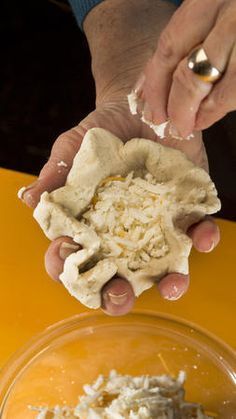 two hands are holding food in front of a yellow counter top and one hand is grabbing something out of a bowl