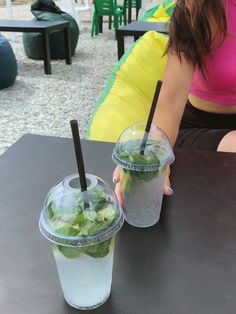 a woman sitting at a table with two cups of ice tea in front of her