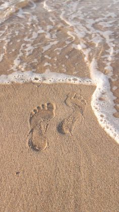 two footprints in the sand next to the water at the beach with waves coming in