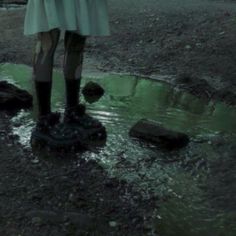 a woman standing on top of a puddle next to a green fire hydrant in the rain