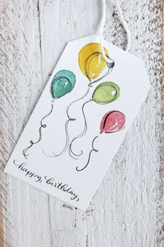 a happy birthday card with balloons hanging from a string on a wooden background, which reads happy birthday